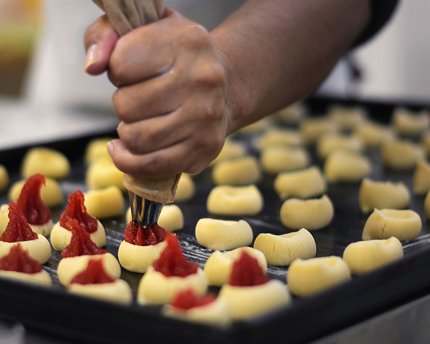 Mão com saco de confeitar colocando goiabada sobre biscoitinhos amanteigados numa assadeira