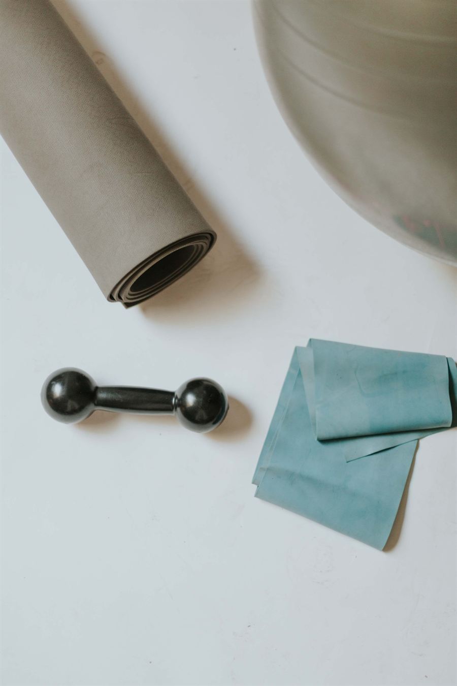 Colchonete enrolado, halter, faixa elástica e bola de pilates sobre o chão claro